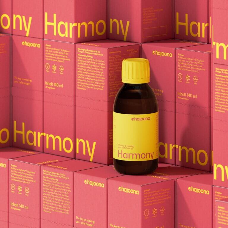 Produktabbildung von hajoona Harmony: Eine braune Flasche mit gelbem Deckel und Etikett, platziert vor einem Hintergrund aus korall- und gelbfarbenen Produktverpackungen. Die Gestaltung wirkt einladend und hochwertig.