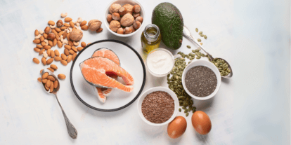Verschiedene Omega 3 reiche Lebensmittel wie Lachs, Avocado, Nüsse, Samen, Eier und Öl liegen dekorativ auf einem hellen Untergrund