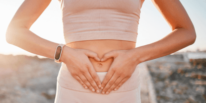 Frau in sportlicher Kleidung formt mit ihren Händen ein Herz über ihrem Bauch – Symbol für Darmgesundheit, Wohlbefinden und Achtsamkeit.