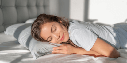 Frau schläft friedlich auf der Seite in einem hellen Bett, mit einem Lächeln im Gesicht.