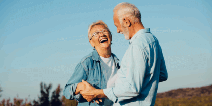Ein älteres Paar lacht herzlich und tanzt gemeinsam im Freien bei Sonnenschein; Continue to the article "Ageing healthily? With a plan!"