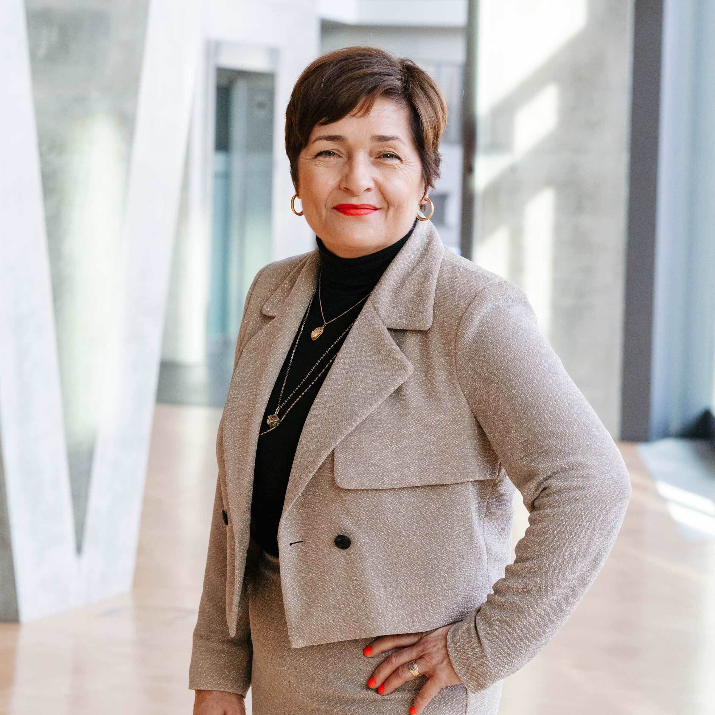 Daniela Lipgens, Geschäftsführerin der hajoona GmbH, steht in einem modernen, lichtdurchfluteten Gebäude und blickt lächelnd in die Kamera.