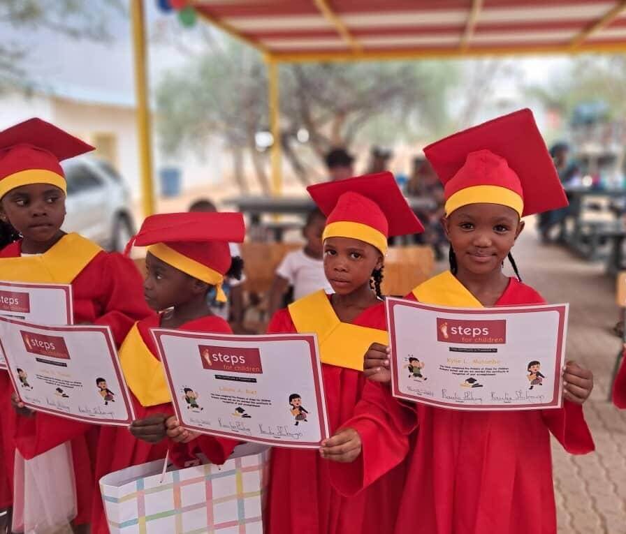 Vier Kinder sitzen an einem Tisch und halten selbst gebastelte Schutzengel-Figuren hoch. Sie lächeln und wirken fröhlich – Symbol für Kreativität, Hoffnung und Förderung im steps-for-children-Projekt.