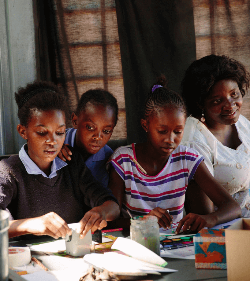 Kinder sitzen gemeinsam an einem Tisch, malen und basteln, während eine Betreuerin sie begleitet – Symbol für Bildung, Kreativität und Förderung im steps-for-children-Projekt.